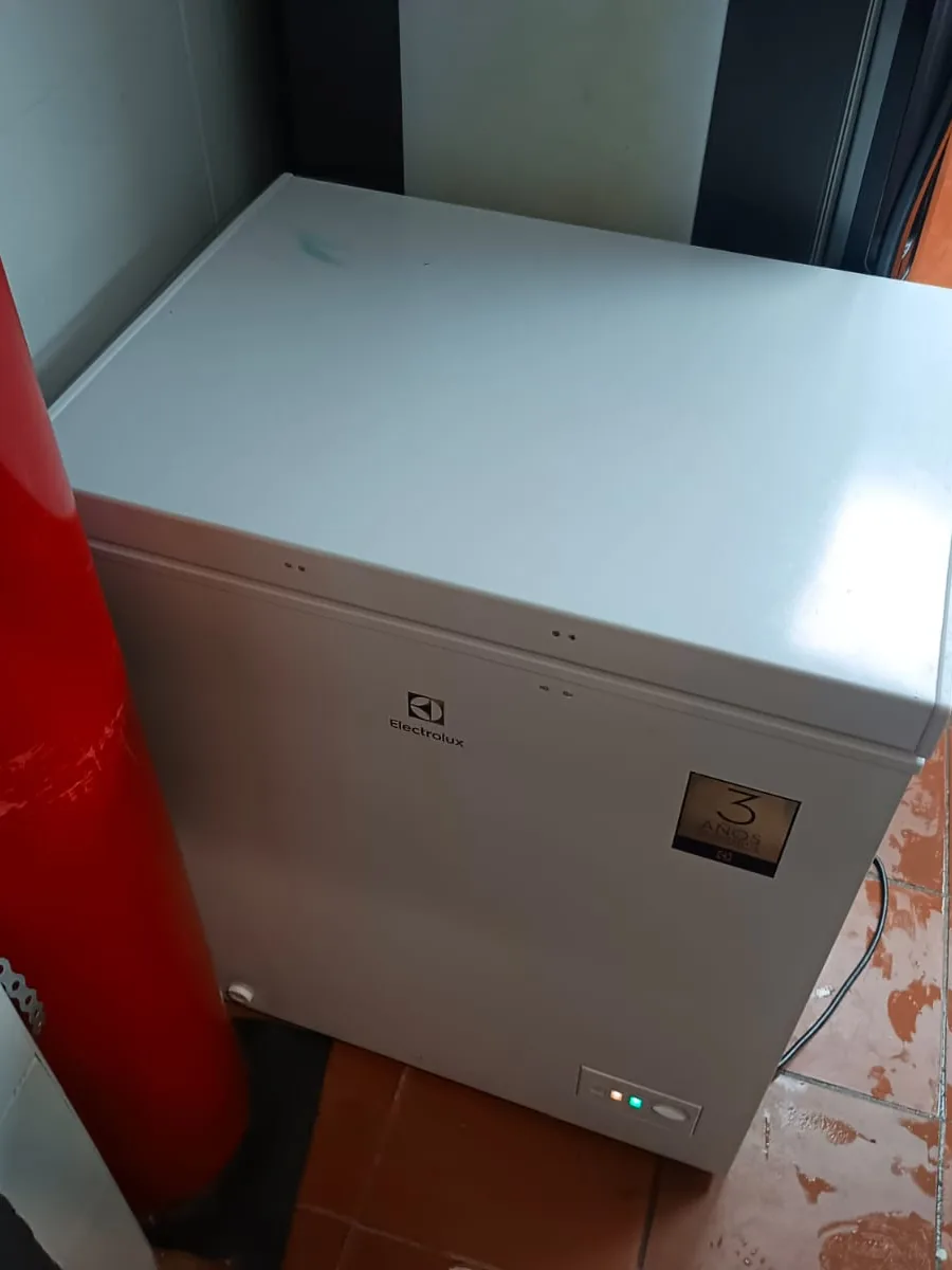 Congelador horizontal blanco junto a un extintor rojo, con el piso mojado