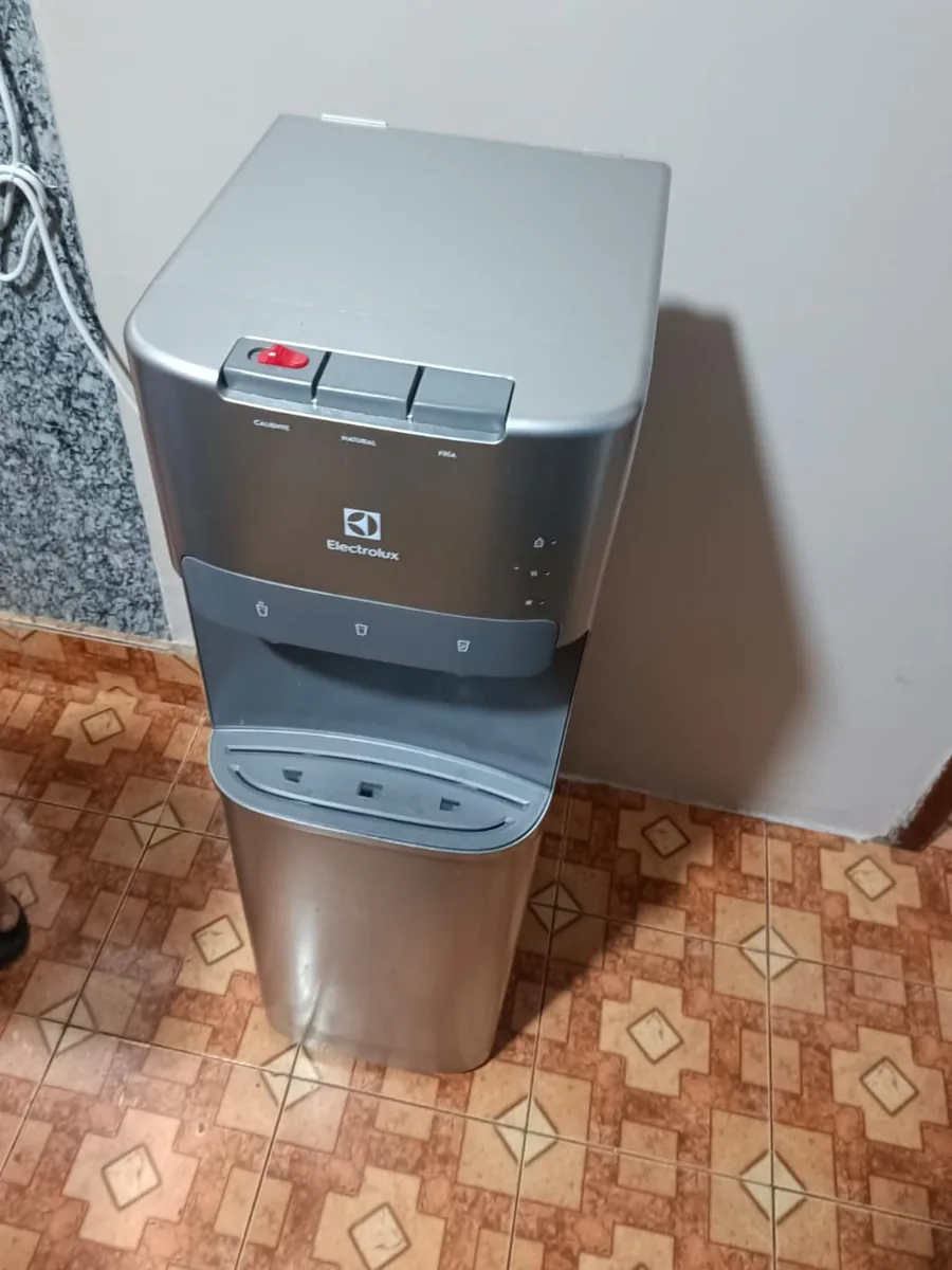 Dispensador de agua gris de pie, con botones en la parte superior, sobre un piso de baldosas