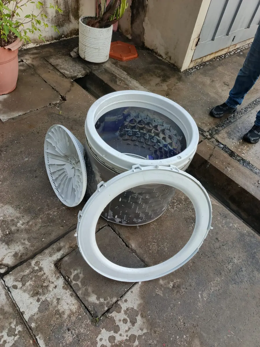 Piezas de una lavadora desarmada sobre el piso de un patio