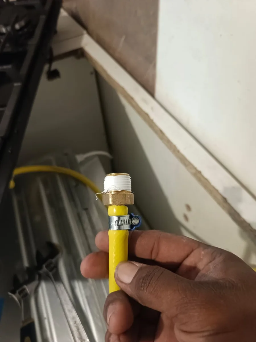 Mano sosteniendo una manguera amarilla con un conector de latón, dentro de un mueble
