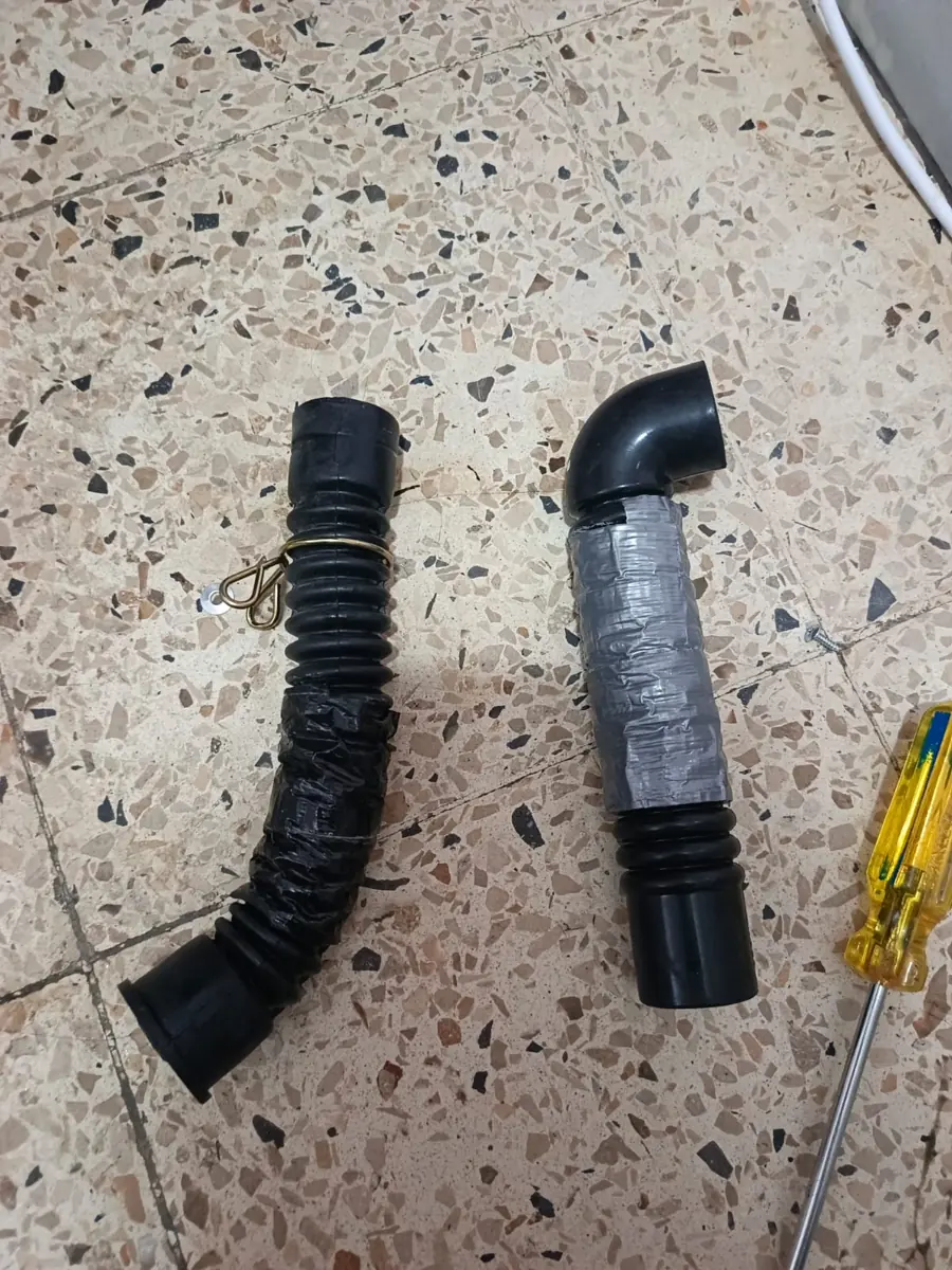 Dos mangueras de desagüe, una con cinta aislante, junto a un destornillador
