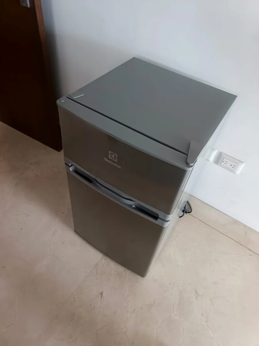 Refrigeradora gris de dos puertas, con el congelador arriba, junto a una pared