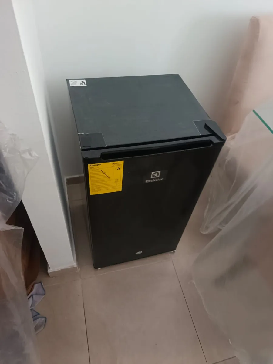 Refrigeradora pequeña negra junto a una pared, con plástico protector alrededor