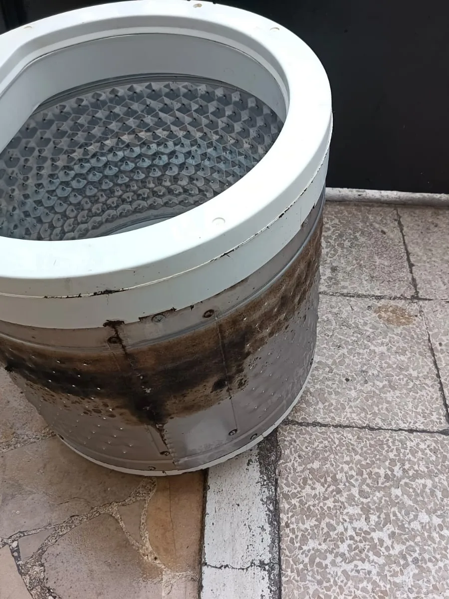Tina de lavadora con manchas oscuras de residuos, apoyada en el piso de un patio